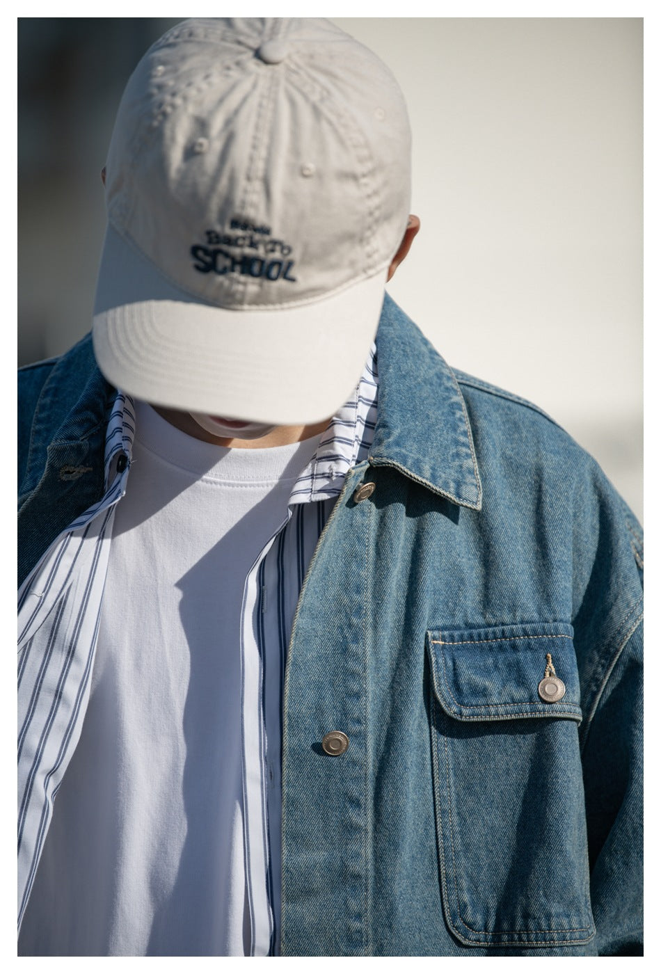 Close view of a model wearing a blue denim jacket with a chest pocket over a striped shirt and white tee.