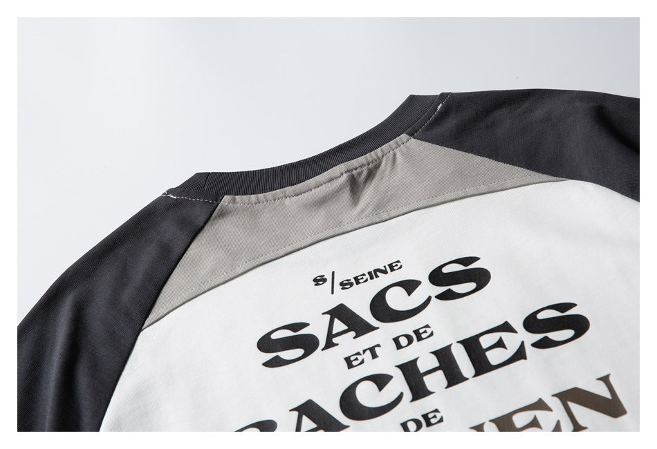 Close-up of the back neckline and gray shoulder panel on a white T-shirt with charcoal sleeves and black lettering.
