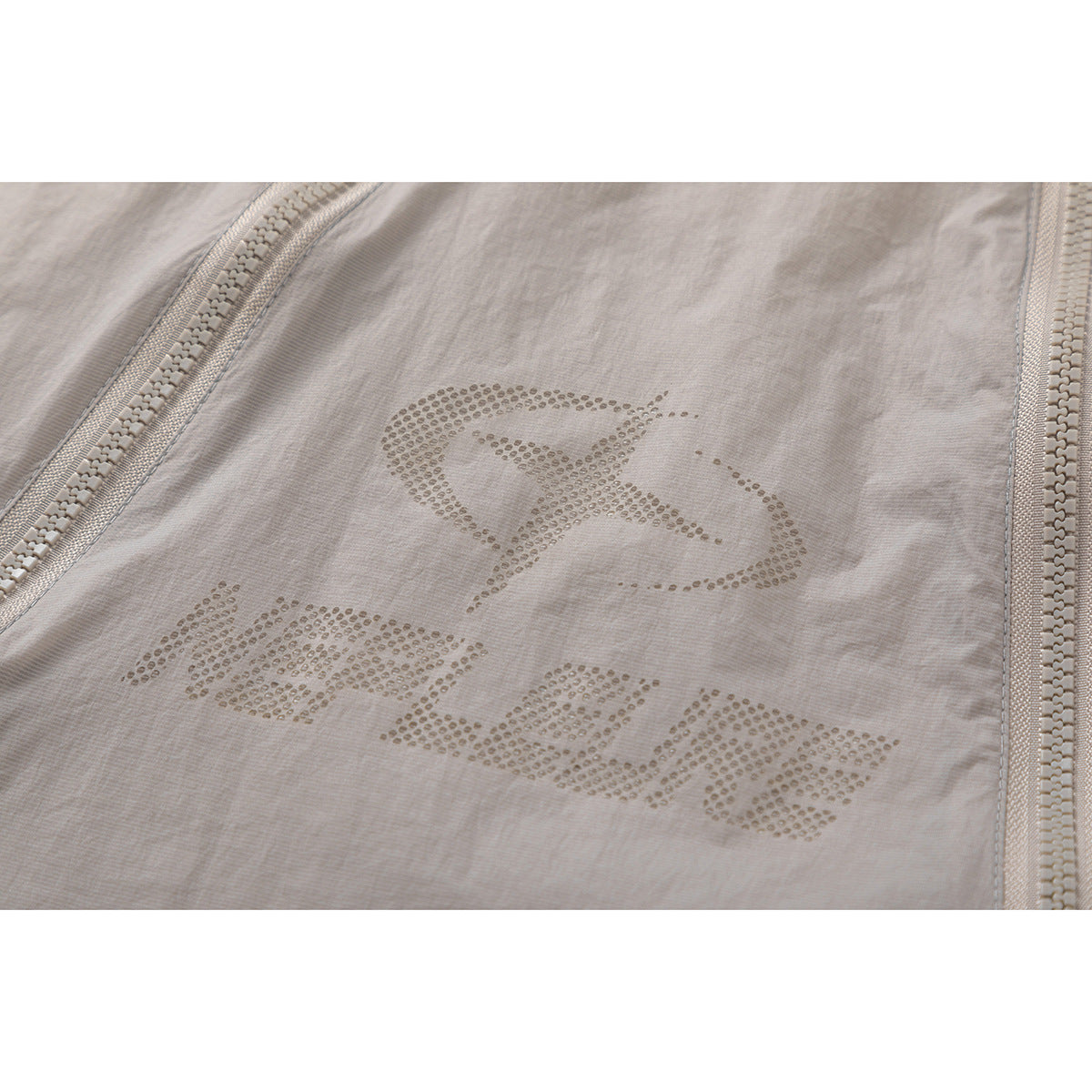 Close-up of dotted graphic lettering on a light taupe jacket, framed by two front zippers.