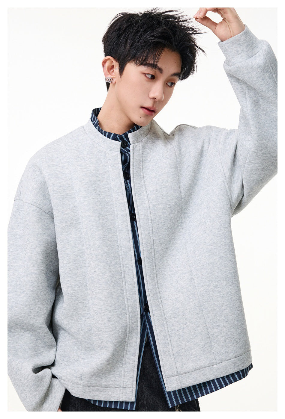 Close view of a model wearing a light gray jacket with a stand collar and dark buttons over a blue striped shirt.