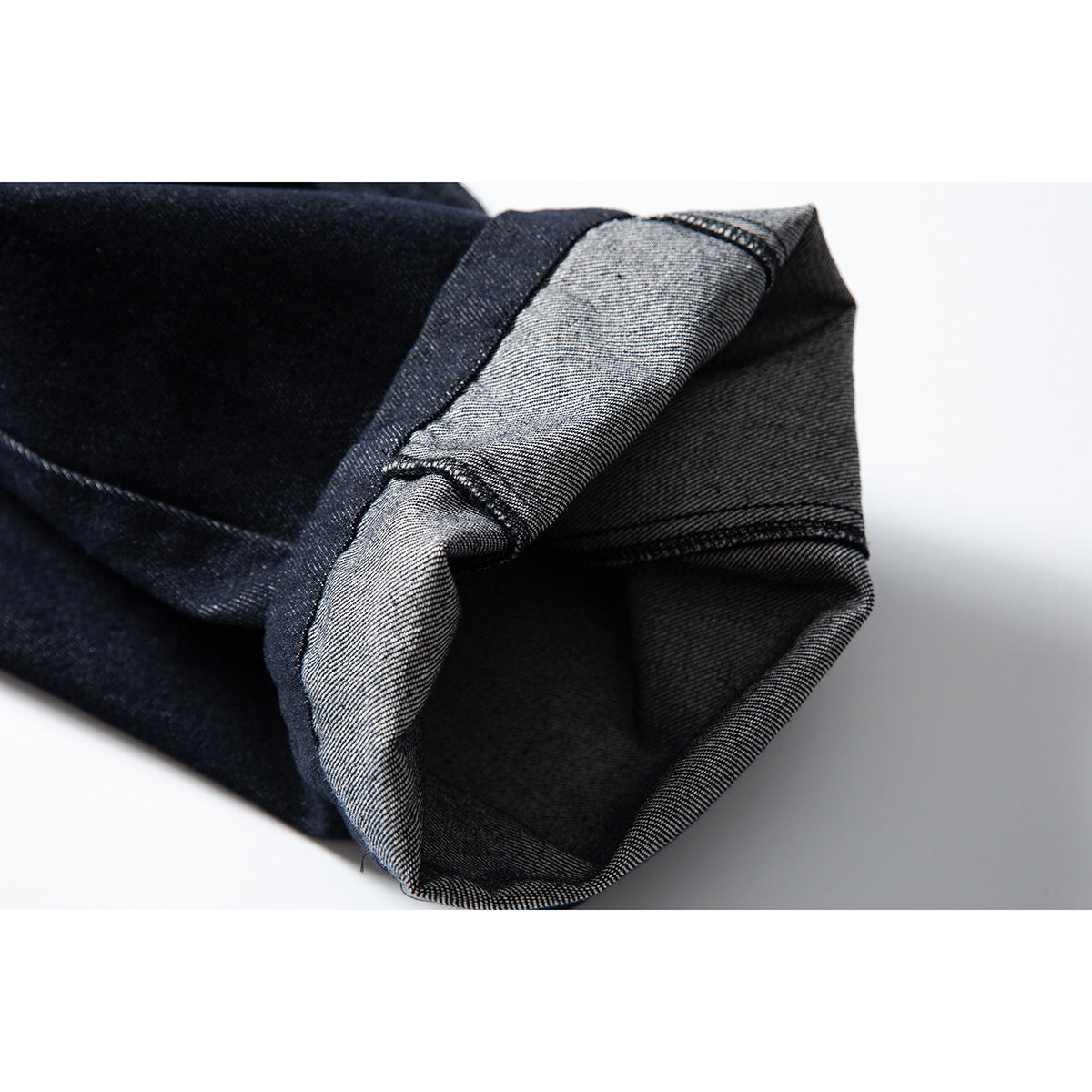 Close-up of a folded pant leg showing the dark denim exterior, lighter reverse side, and stitched hem.