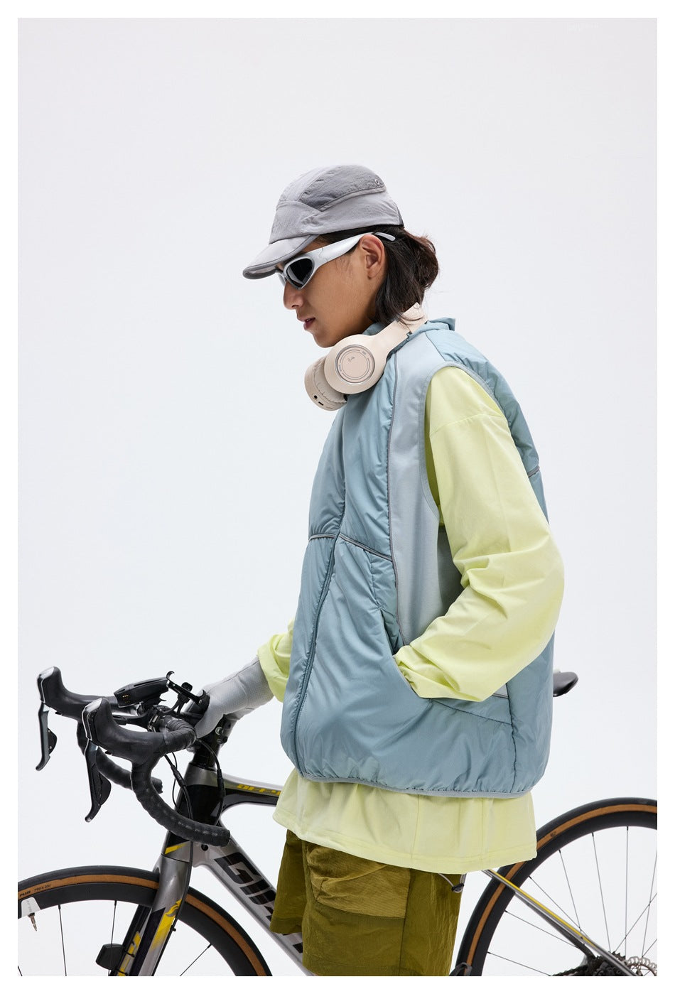 Side view of a cyclist wearing a pale blue zip-front vest with light reflective trim.