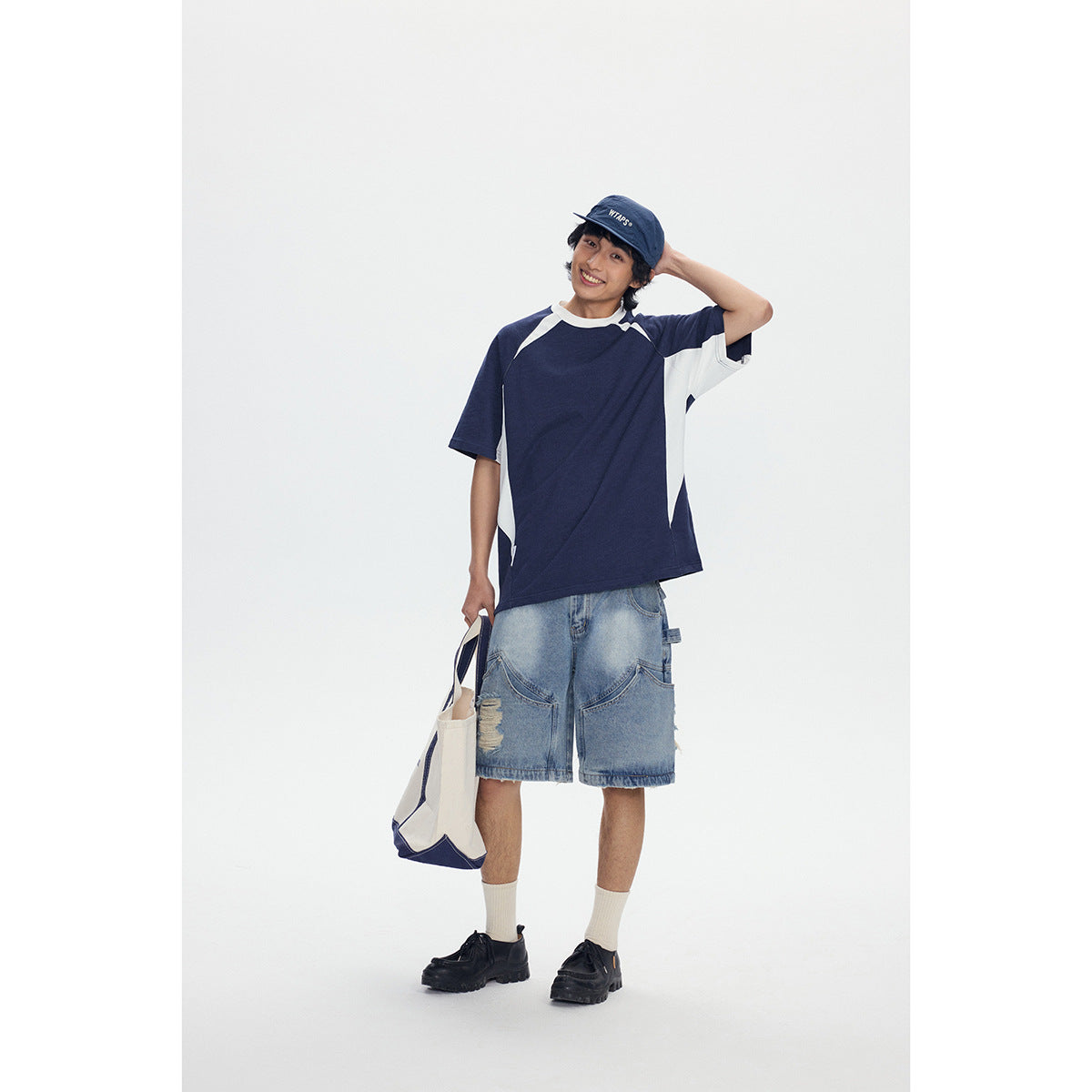 Model wearing a navy and white raglan T-shirt with light-wash denim shorts, shown from the front.