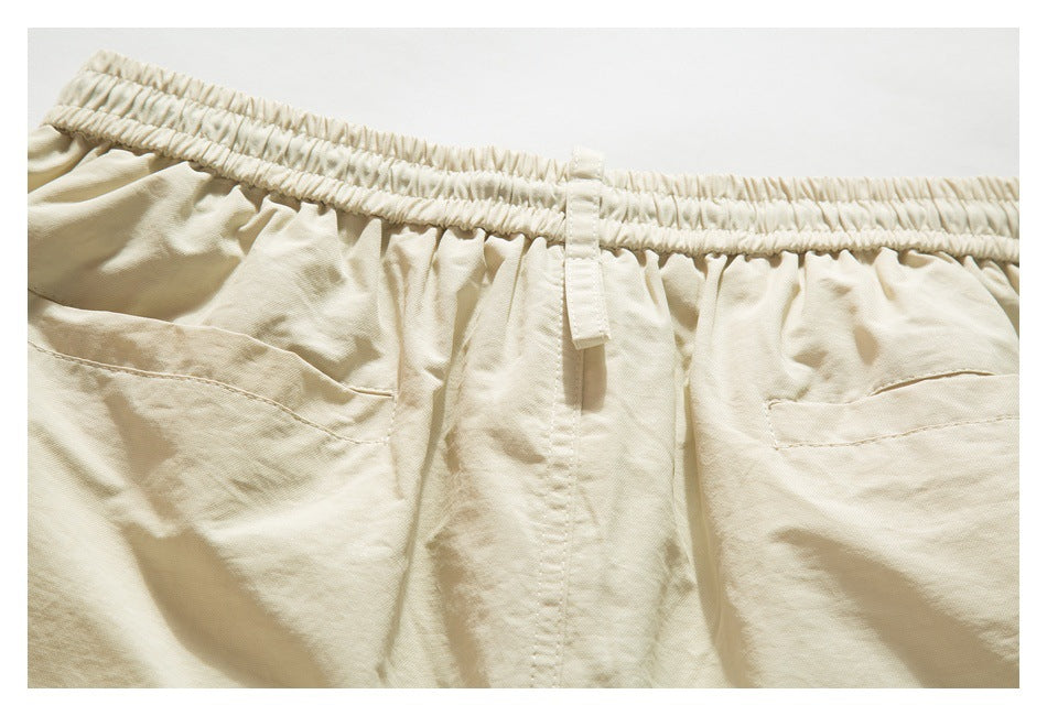 Close-up of cream-beige trousers showing a gathered elastic waistband, belt loop, and two rear pockets.