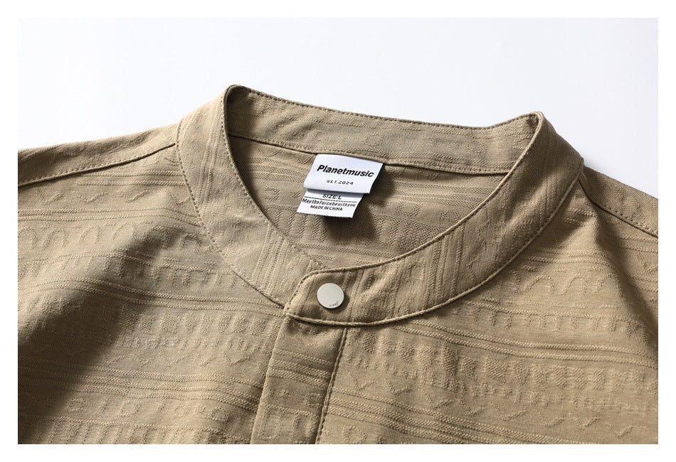 Close-up of the tan shirt's band collar, top button, textured fabric, and sewn-in neck labels.