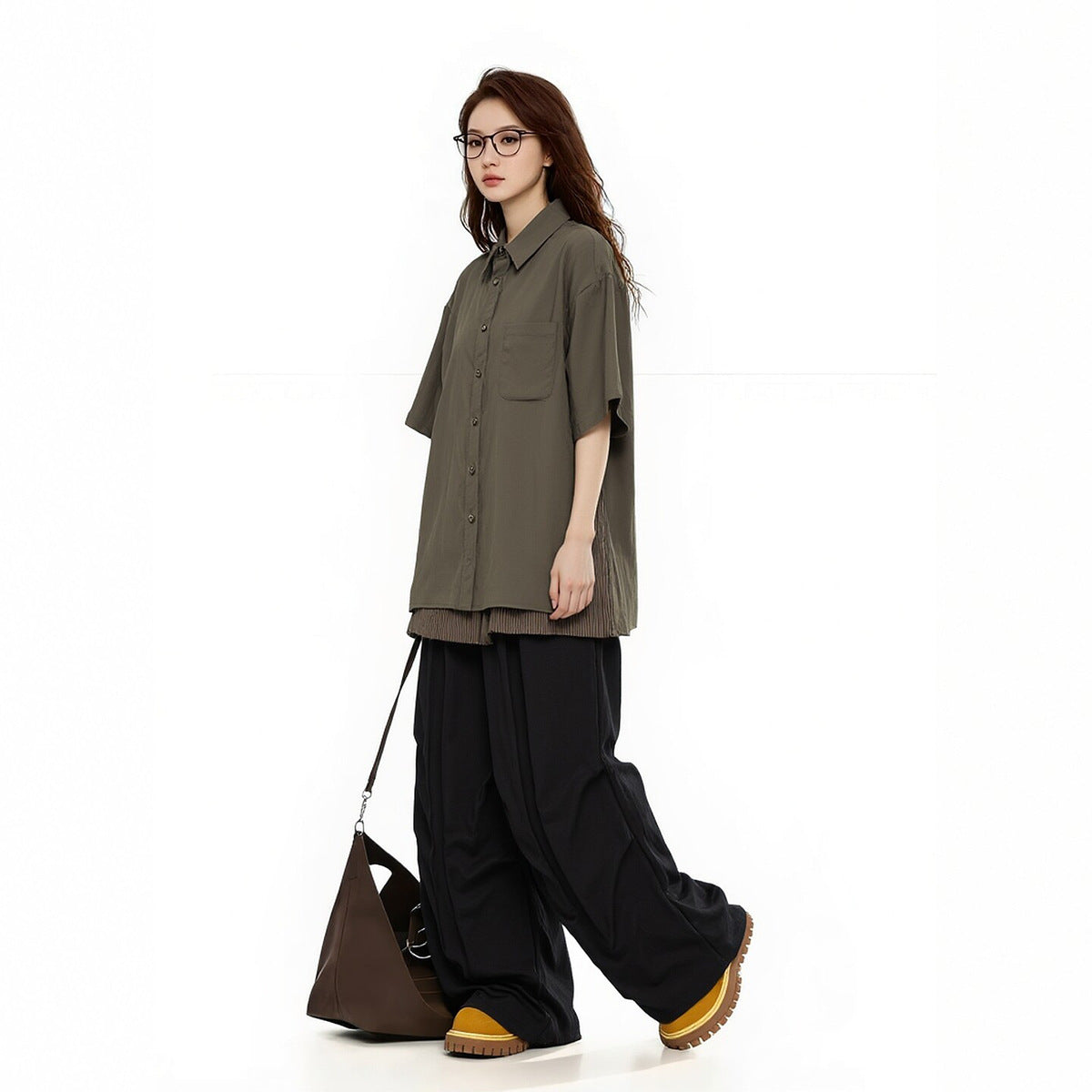 Woman in an olive short-sleeve button-up shirt with a chest pocket and loose black trousers, shown at an angle.