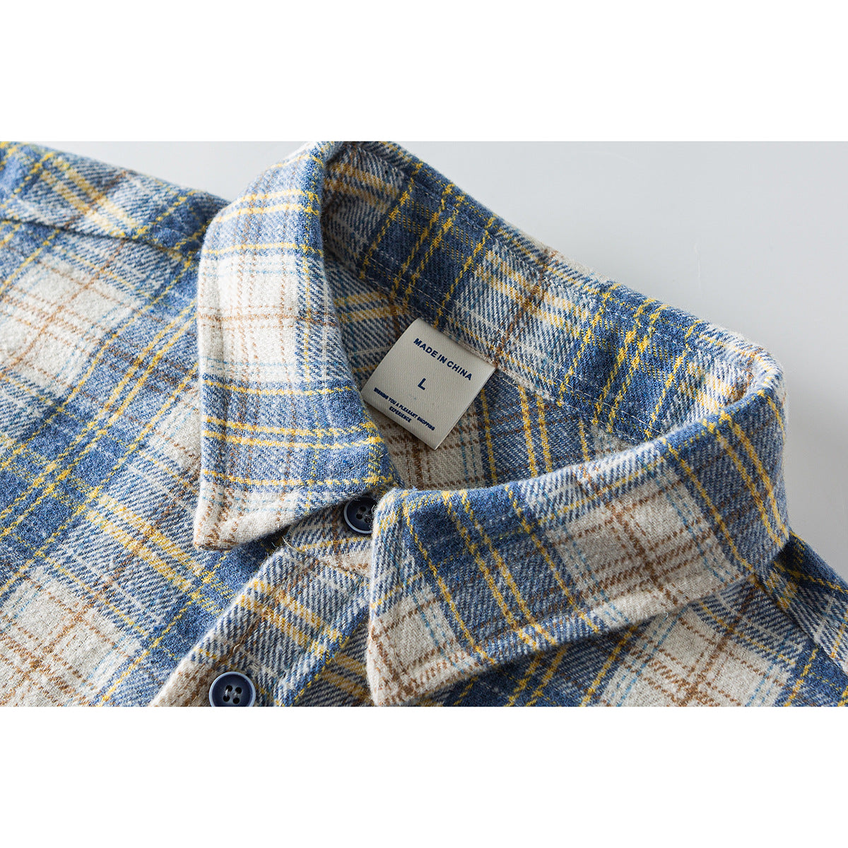 Close-up of a blue, cream and yellow plaid shirt collar with dark buttons and a size label.