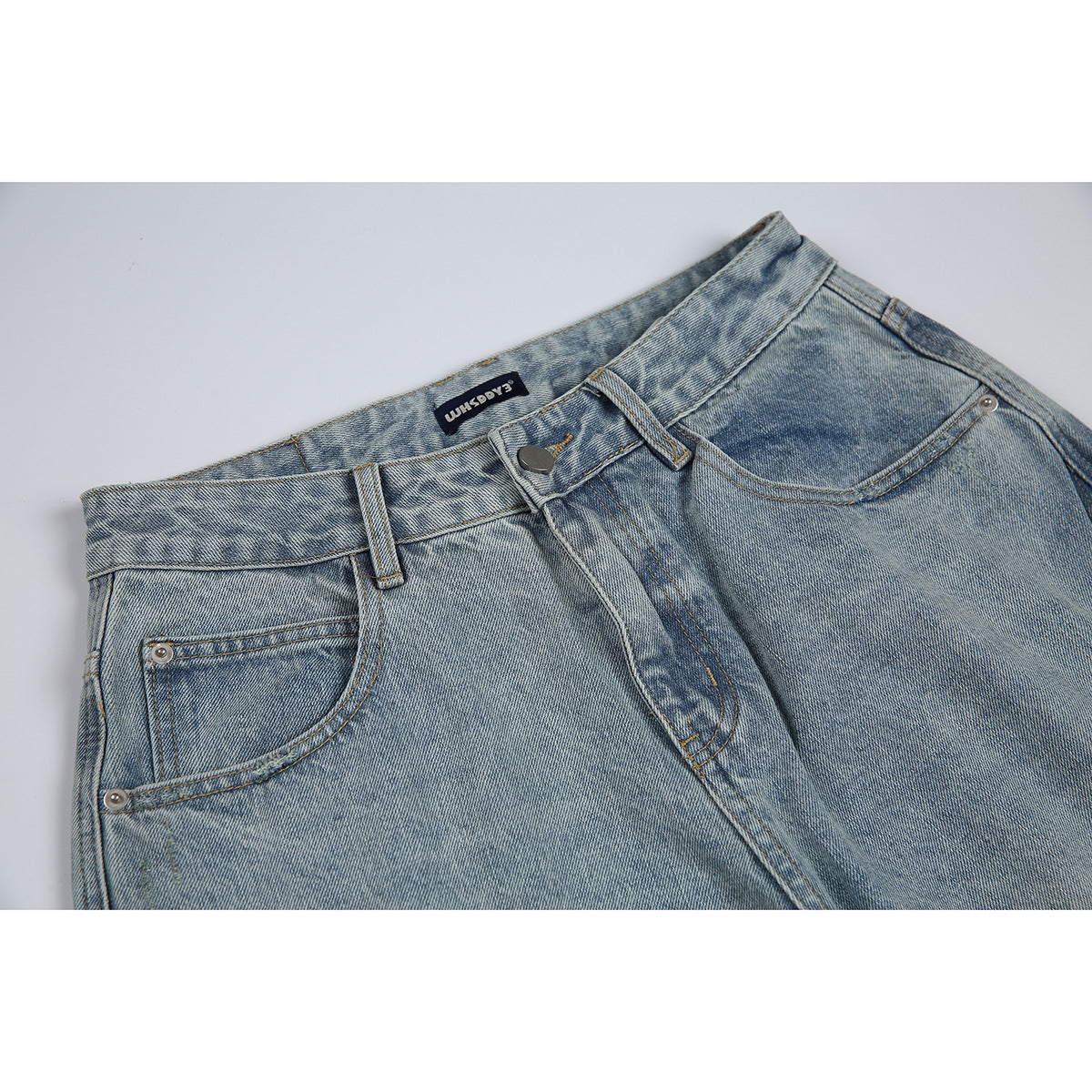 Close-up of light blue washed jeans showing the front waistband, button, belt loops, and front pockets.