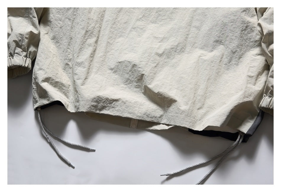 Close-up of a light beige garment hem with adjustable drawcords and elasticized sleeve cuffs.