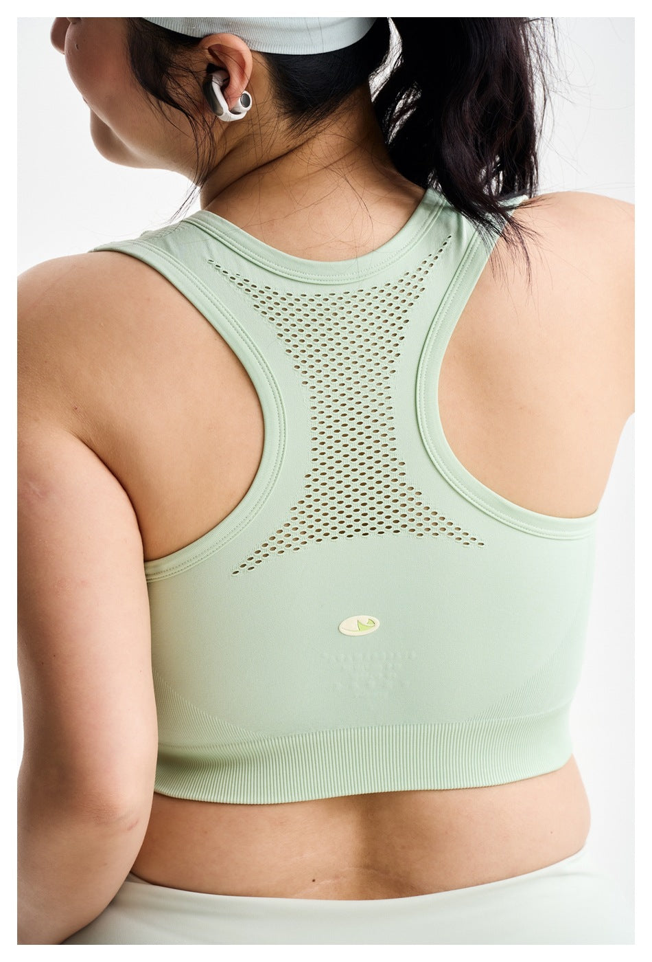 Close rear view of a model wearing a pale mint racerback sports bra with a perforated mesh-like back panel.