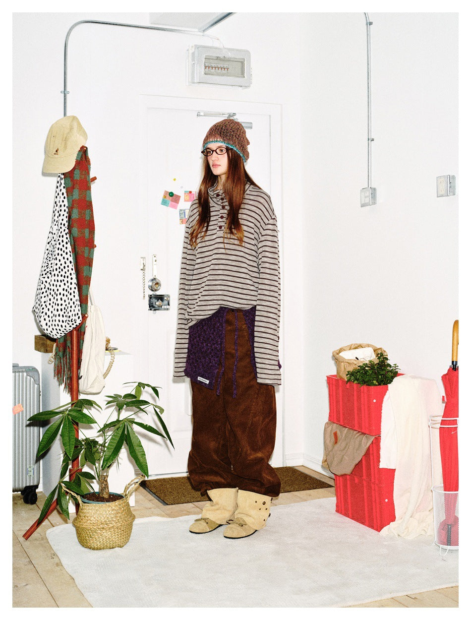 Three-quarter view of a model in a gray striped long-sleeve top, brown trousers, purple waist wrap, and knit beanie.