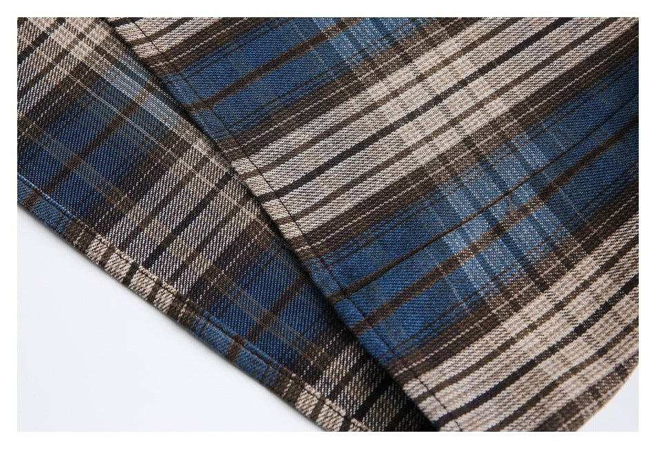 Close-up of a stitched seam and overlapping panels on the blue, brown, and cream plaid shirt.