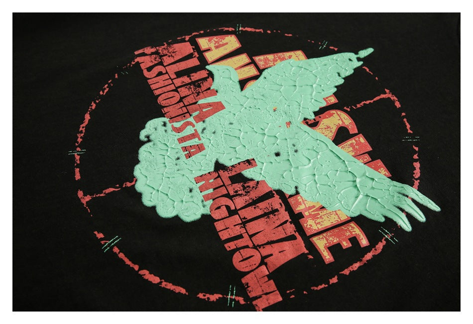 Close-up of a raised mint-green eagle over distressed red and yellow lettering on a black T-shirt.