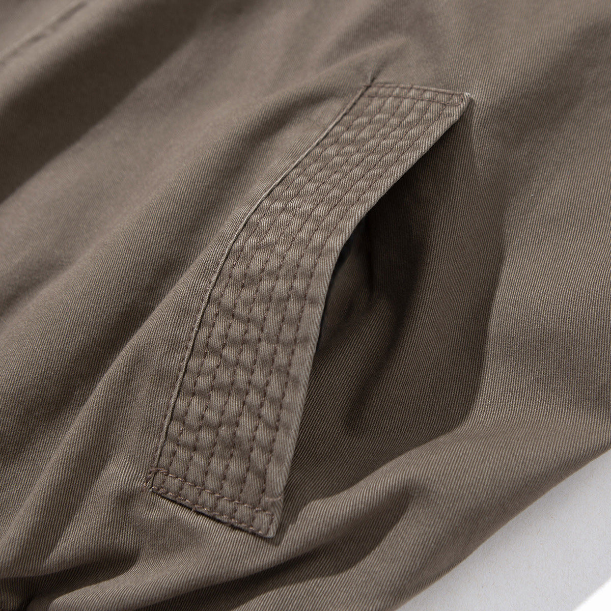 Close-up of a brown-gray jacket showing a long, densely stitched fabric panel and seams.