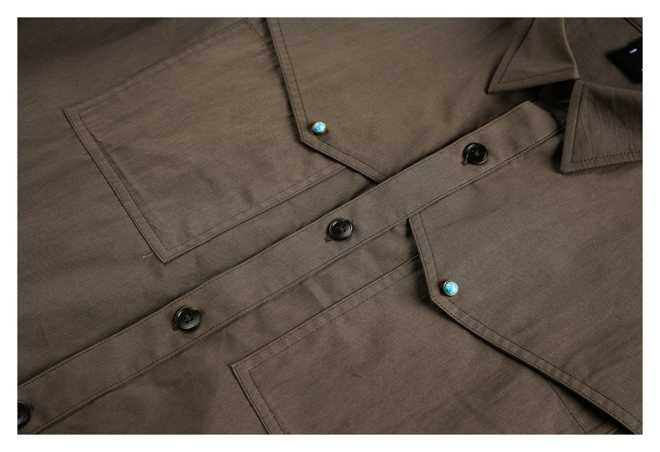 Close-up of a brown shirt front with two patch pockets, black buttons, and turquoise pocket-flap buttons.