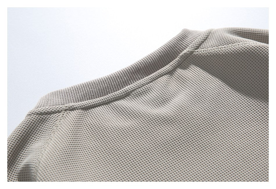 Close-up of the ribbed crew neckline and waffle-knit fabric of a taupe garment.