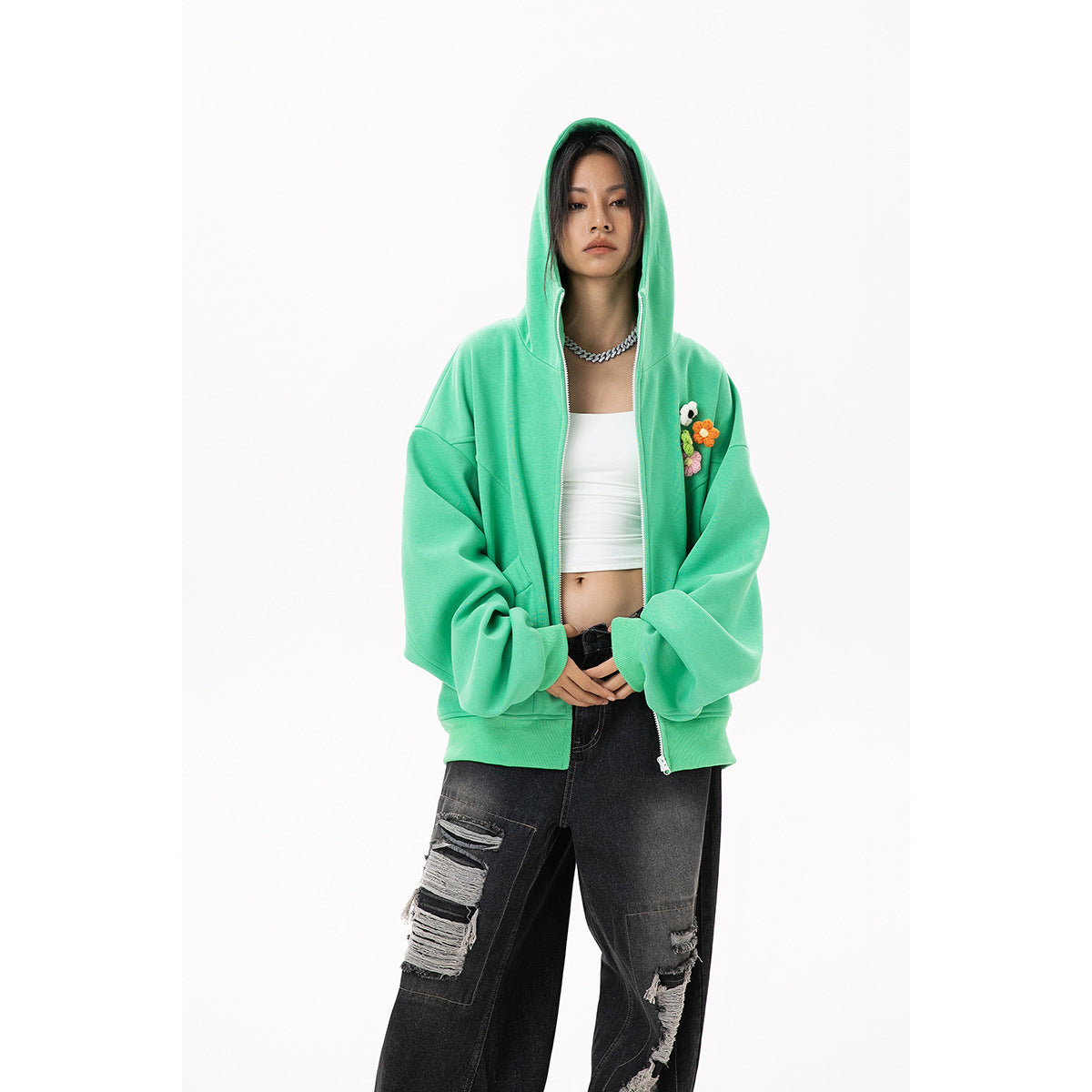 Front view of a model wearing a mint-green hooded zip-up with flower appliqués and distressed black jeans.