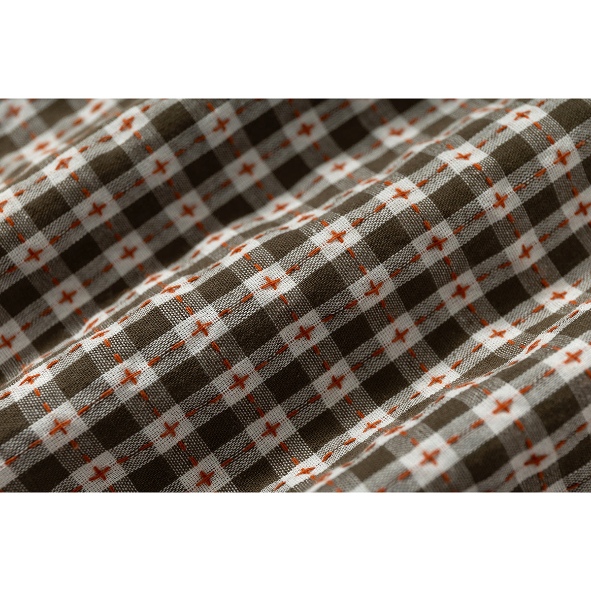 Macro view of brown and white plaid fabric with rust-colored cross and dash stitching.