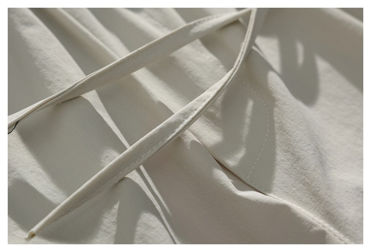 Close-up of off-white garment fabric with narrow stitched drawstrings crossing over a seam.