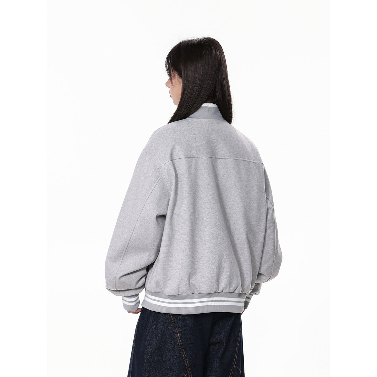Rear view of a model wearing a light gray oversized bomber jacket with a plain back and striped ribbed cuffs and hem.