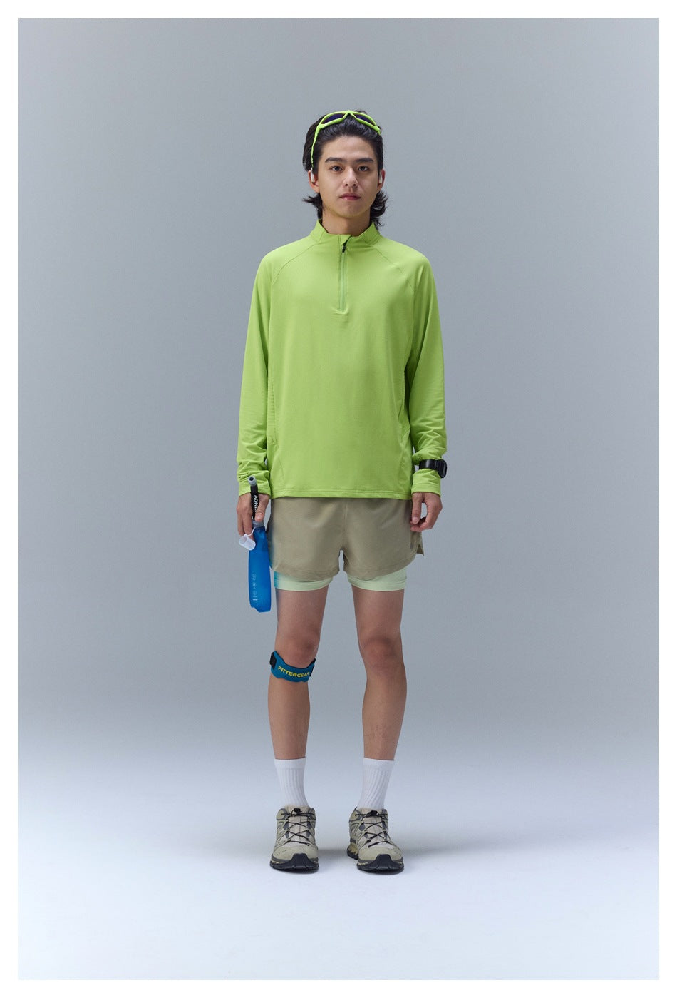 Person wearing lime green quarter-zip long-sleeve top with beige shorts, facing front in a studio