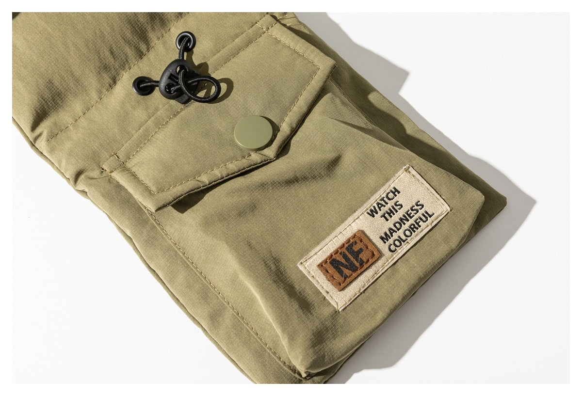 Olive garment detail with a snap-fastened flap, black cord toggle, and sewn English text patch.