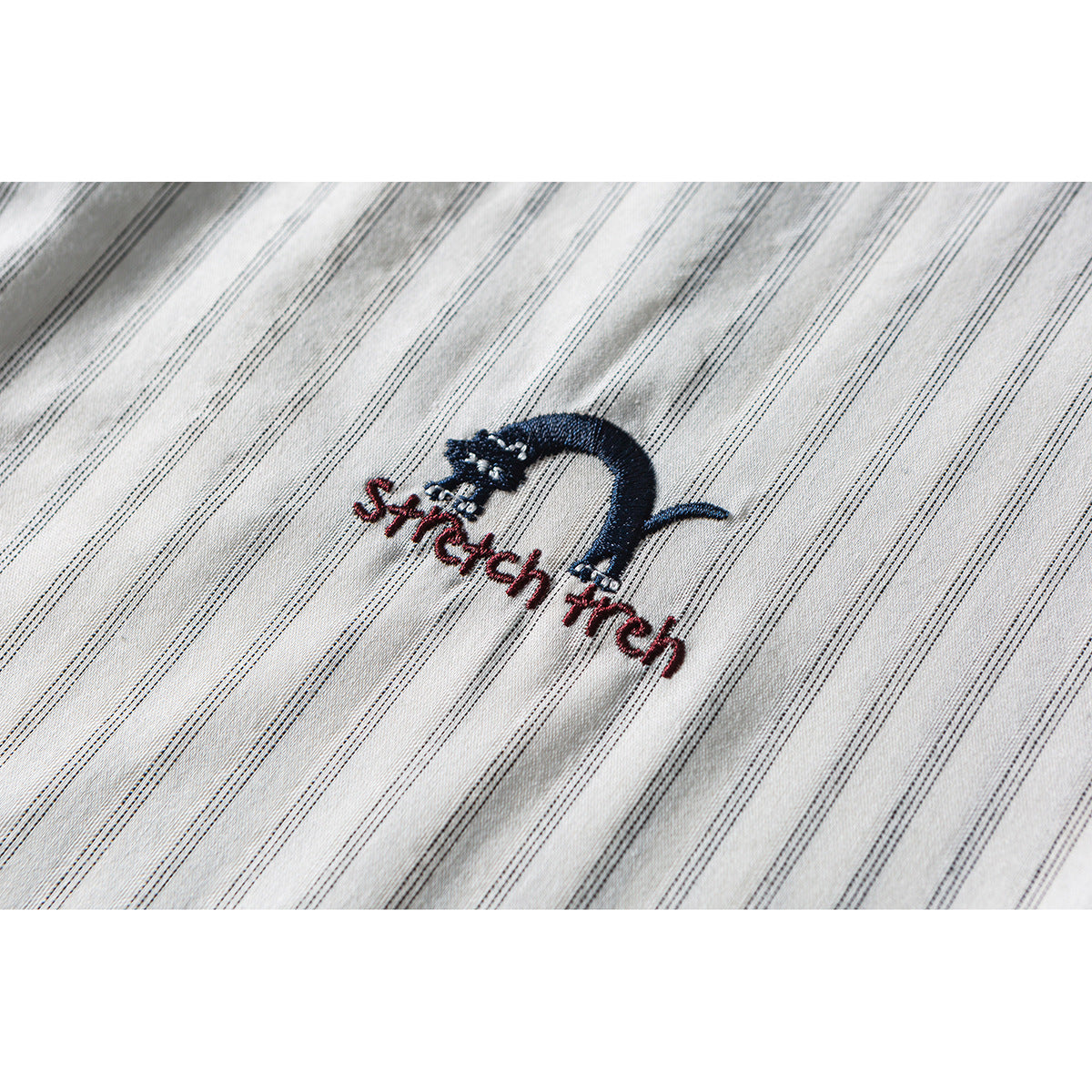 Close-up of embroidered navy and red lettering on cream fabric with fine dark stripes.