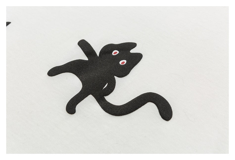 Close-up of a black stylized animal graphic with red-and-white eyes on off-white fabric.