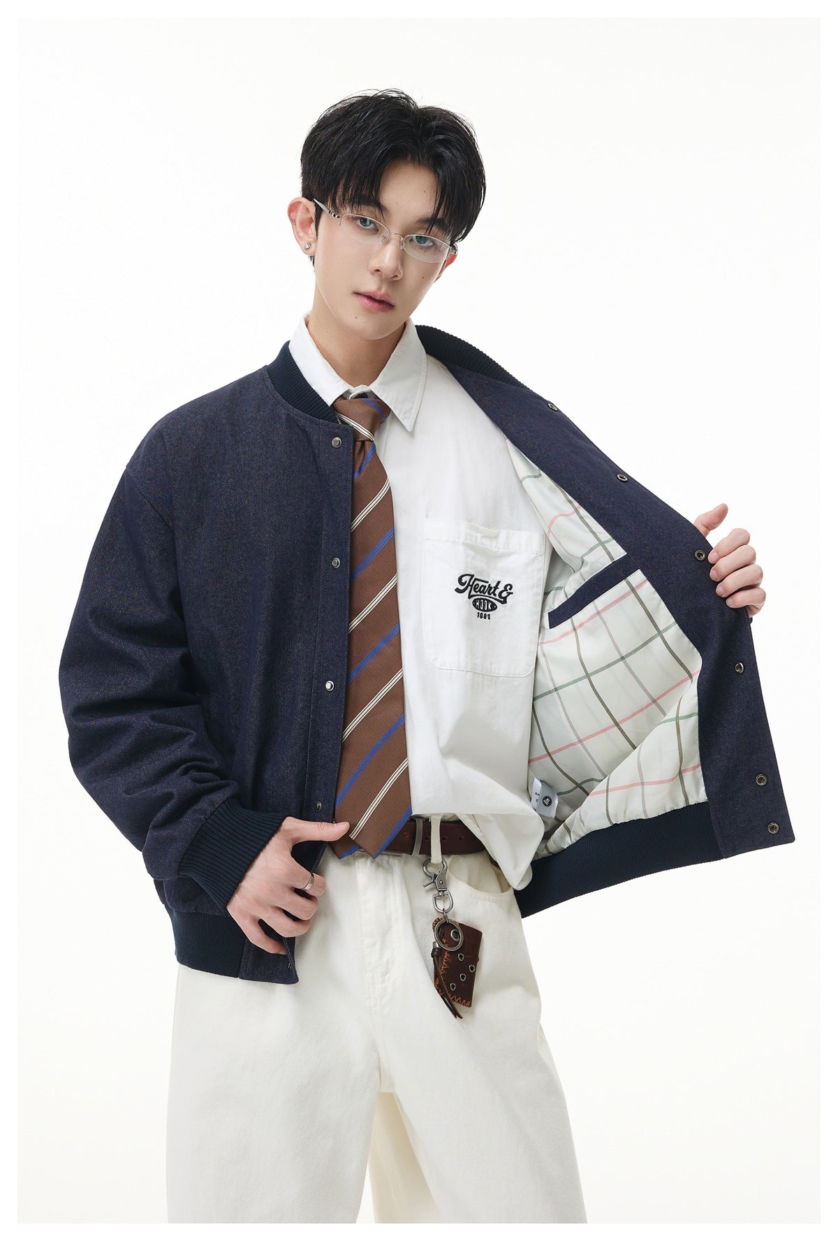 Model holds open a dark navy bomber jacket, revealing its pale plaid lining and a white shirt with embroidered text.