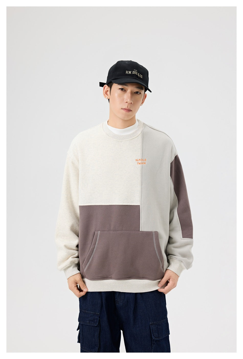 Front view of a model wearing a cream and taupe color-block crewneck sweatshirt with a large front pocket.