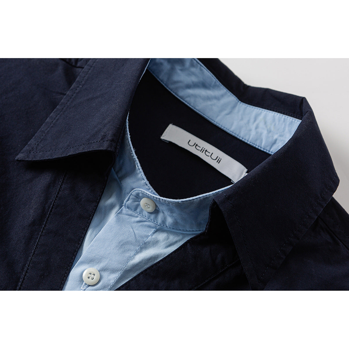 Close-up of a dark navy shirt collar with pale blue inner placket, white buttons, and a sewn neck label.