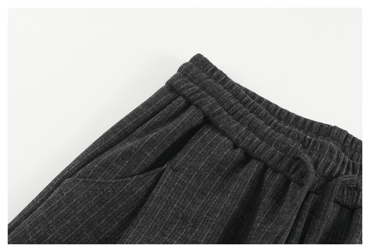 Close-up of charcoal pinstripe trousers showing the elastic waistband, drawstring, and side pocket opening.
