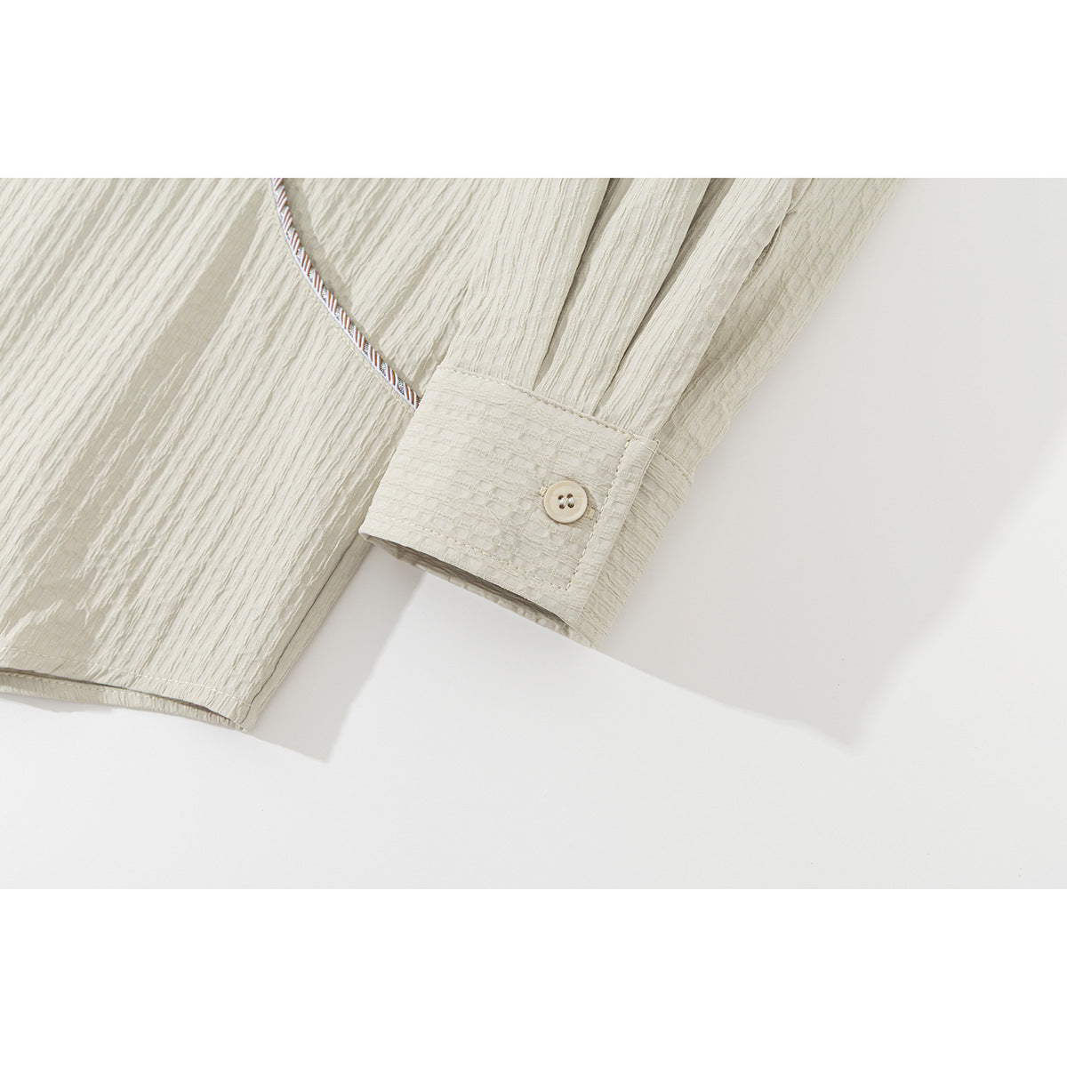 Close-up of a light beige shirt sleeve cuff with a button and contrast piping on textured fabric.