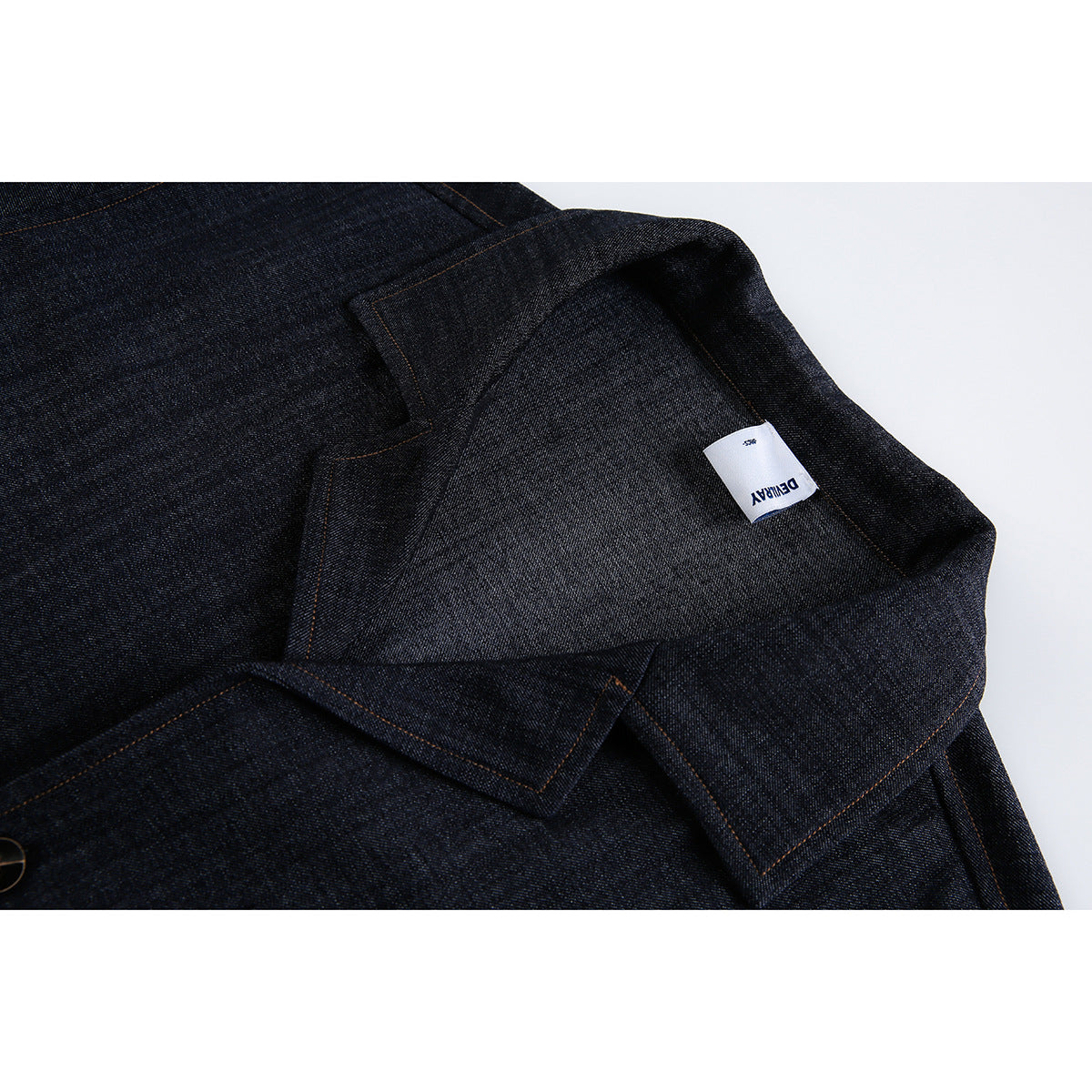 Close-up of dark indigo denim with orange stitching and a small white sewn-in label.