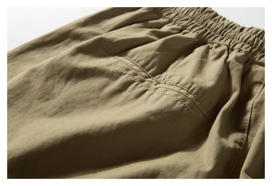 Close-up of a stitched pocket opening below the gathered waistband of khaki trousers.