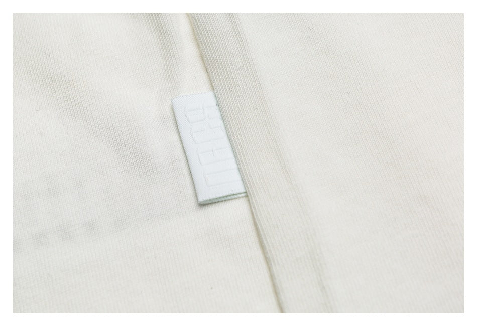 Close-up of off-white fabric with a small white woven tag bearing faint embossed lettering.