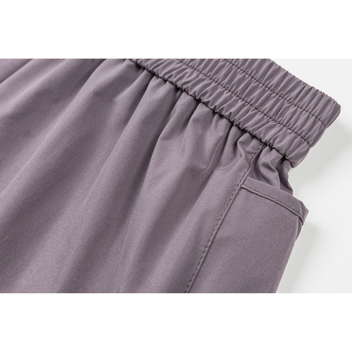 Close-up of mauve-gray shorts showing the gathered elastic waistband and side pocket stitching.