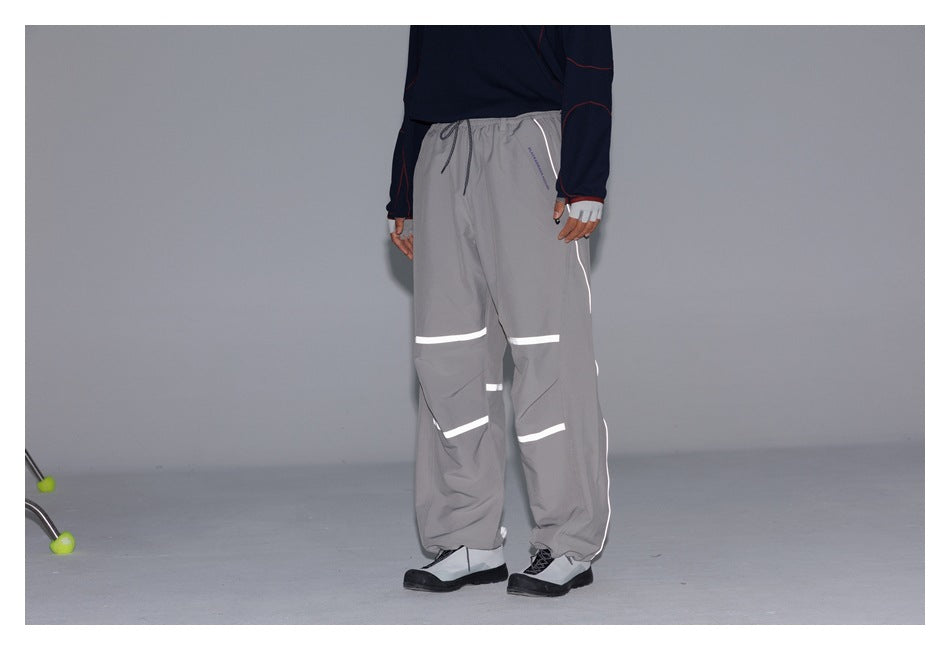 Cropped model wearing gray loose-fit drawstring pants with bright reflective stripes across the legs and along the sides.
