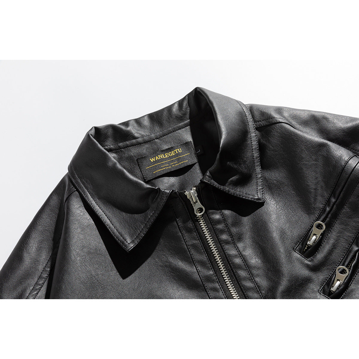 Close-up of a black jacket with a wide pointed collar, silver front zipper, two zip pockets, and a visible neck label.