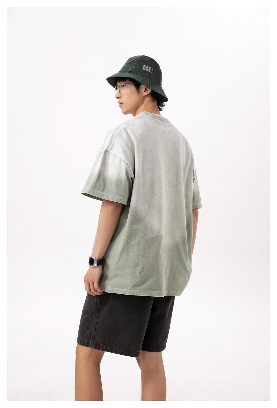 Rear view of a model wearing an oversized pale sage-gray T-shirt with dropped shoulders.