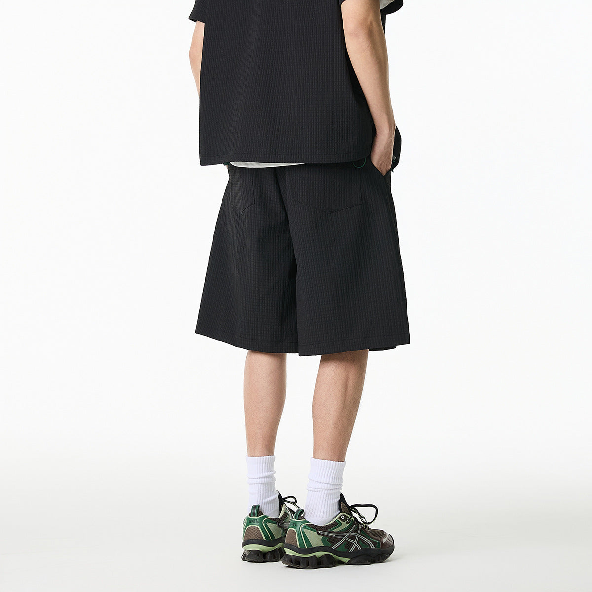 Cropped rear view of a model wearing a black textured shirt and matching knee-length shorts.