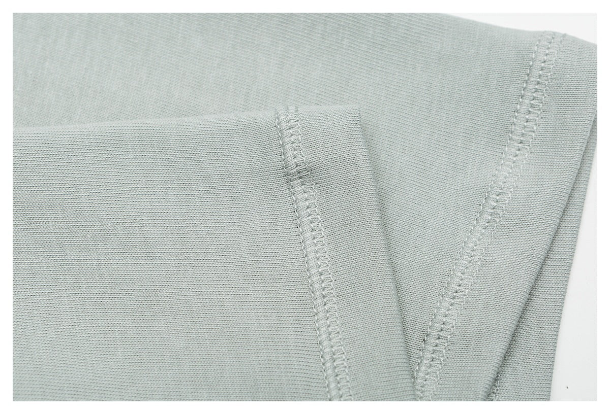Close-up of a folded edge and overlocked stitching on pale sage-gray knit fabric.