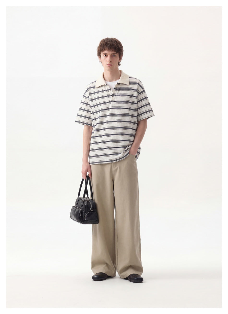 Full-length view of a man wearing an ivory and navy striped polo with beige trousers.