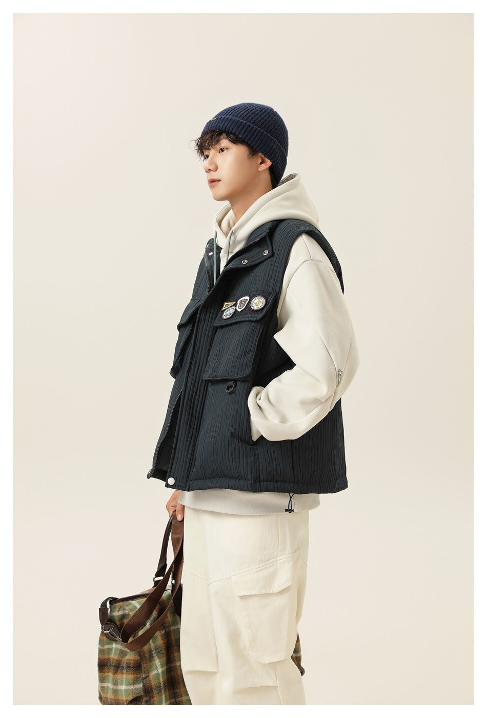 Side view of a model wearing a dark charcoal quilted utility vest over an ivory hoodie.