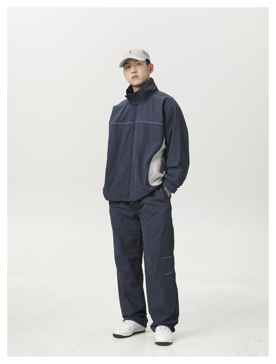 Man in a cap, navy track jacket with gray side panels and navy wide-leg pants with white sneakers