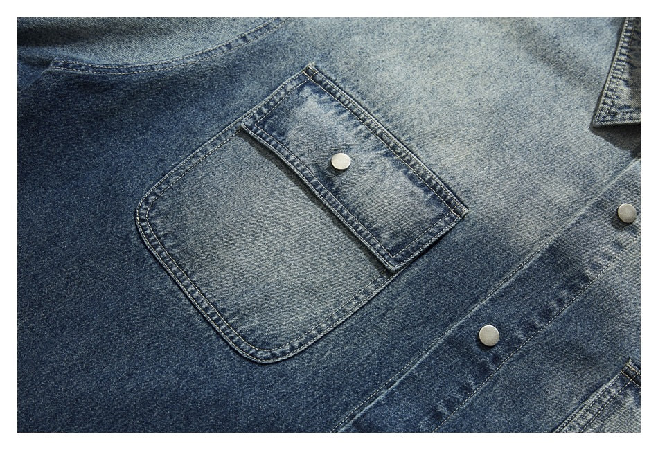 Close-up of a washed blue denim shirt's flap chest pocket, snap buttons, and stitching.