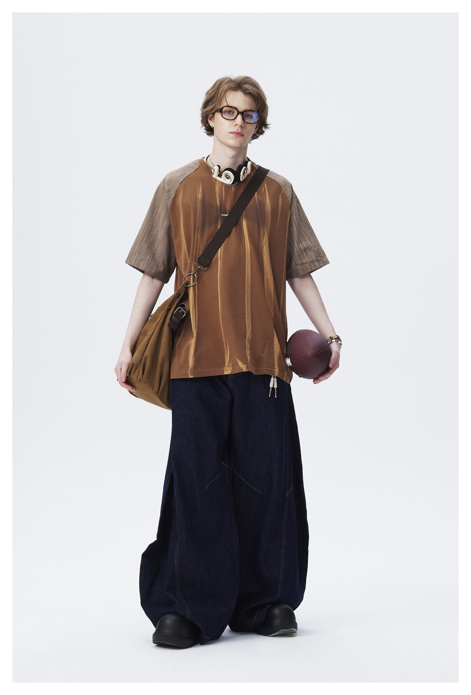 Model wearing brown raglan T-shirt with streaked body and striped sleeves, with wide dark denim pants and a shoulder bag