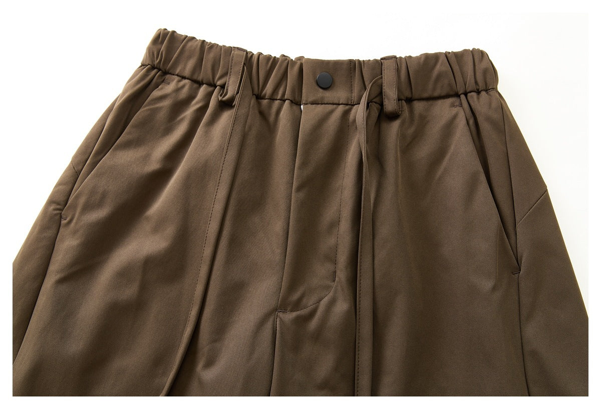 Close-up of brown pants showing an elastic waist, button, drawstring, belt loops, and angled pockets.