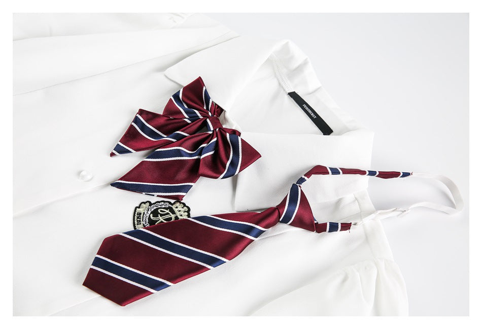Close-up of a white shirt collar, burgundy-and-navy striped bow and crest, with a matching striped tie laid across it.