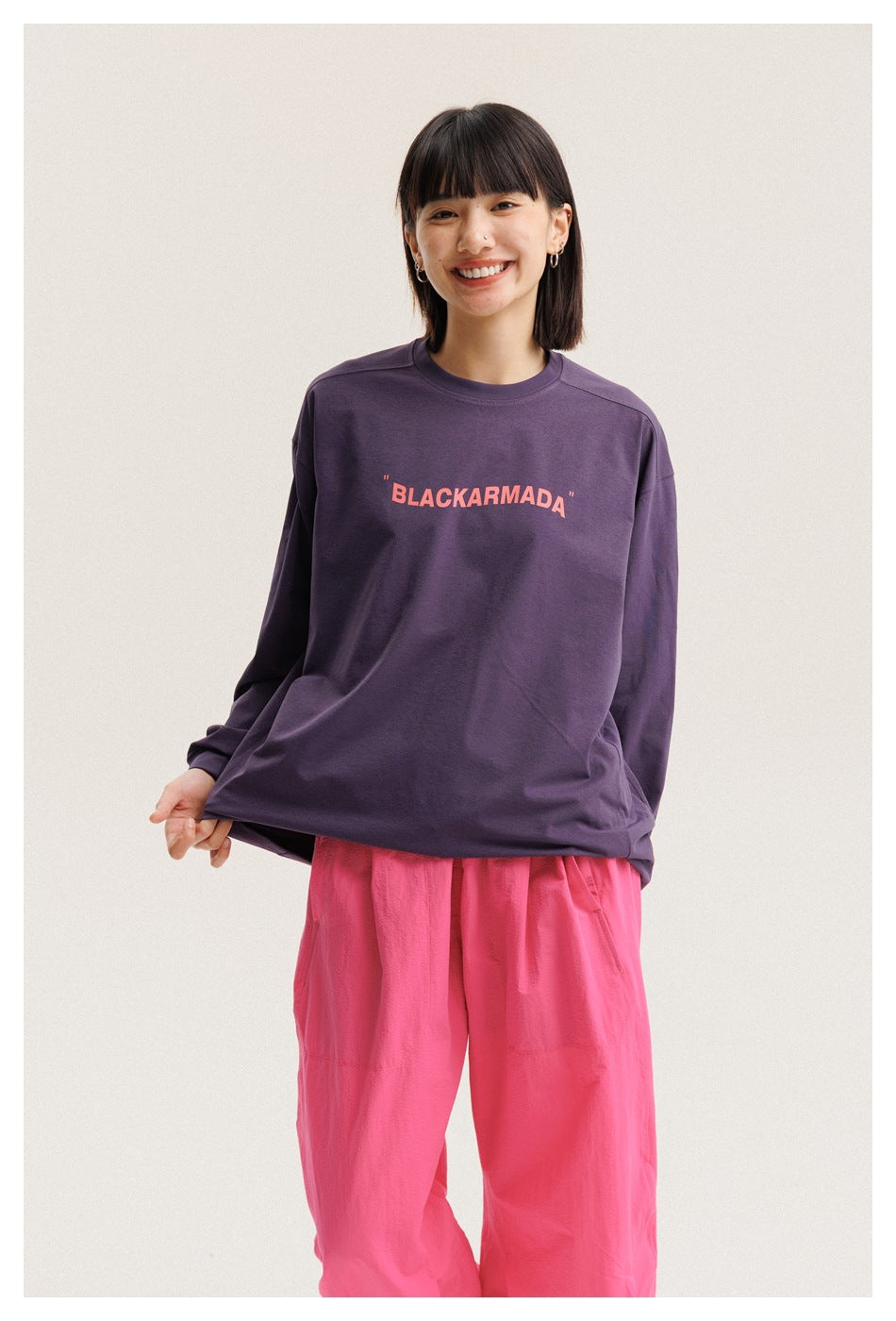 Closer front view of a model wearing a plum long-sleeve T-shirt with coral BLACKARMADA lettering and bright pink pants.